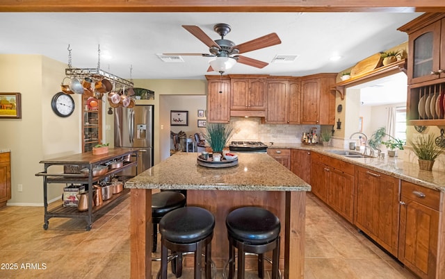 kitchen with a sink, a ceiling fan, stainless steel fridge, under cabinet range hood, and decorative backsplash