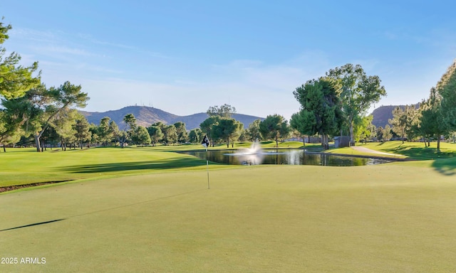 view of home's community with a water and mountain view, view of golf course, and a yard
