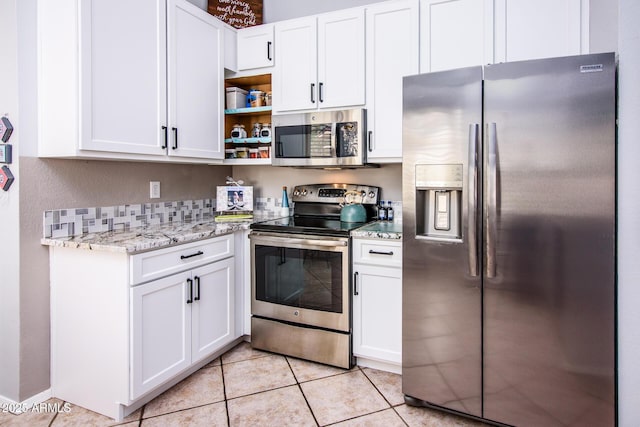 kitchen featuring light tile patterned floors, appliances with stainless steel finishes, white cabinetry, and light stone counters