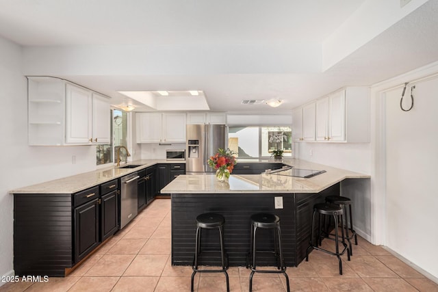 kitchen featuring a peninsula, a sink, white cabinetry, a kitchen breakfast bar, and appliances with stainless steel finishes