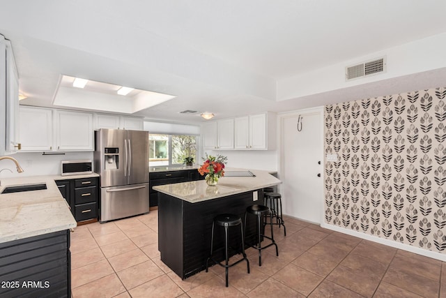 kitchen with a tray ceiling, visible vents, appliances with stainless steel finishes, a sink, and light stone countertops