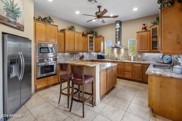 kitchen with wall chimney range hood, sink, light stone countertops, a kitchen island, and stainless steel appliances