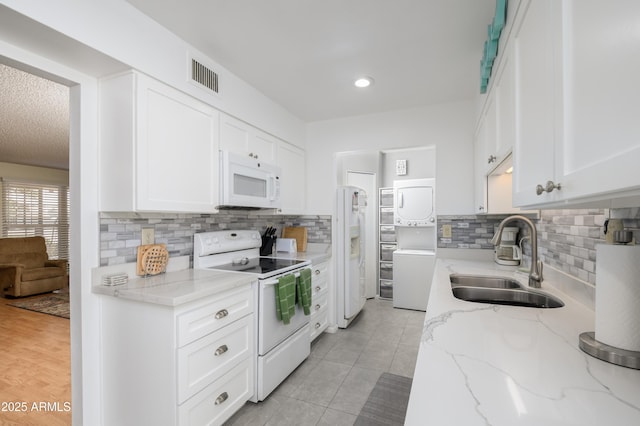 kitchen with sink, white cabinetry, light stone counters, white appliances, and stacked washing maching and dryer