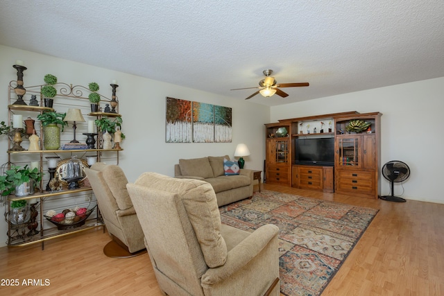 living room with ceiling fan, a textured ceiling, and light wood-type flooring