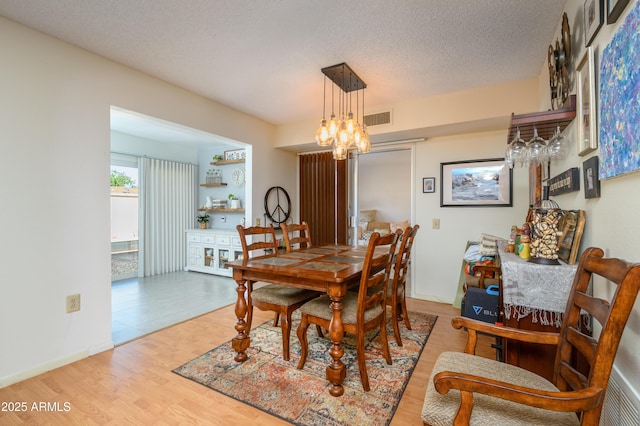 dining room featuring an inviting chandelier, light hardwood / wood-style floors, and a textured ceiling