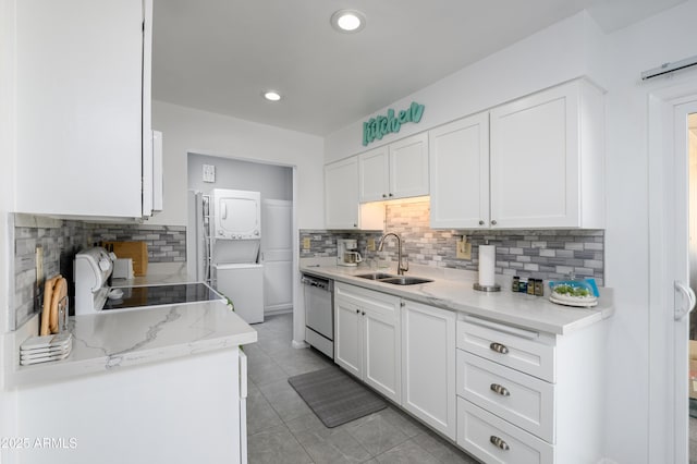 kitchen featuring sink, dishwasher, range, stacked washer / dryer, and white cabinets