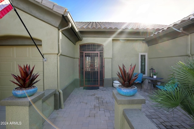 view of exterior entry featuring a tile roof, a patio, an attached garage, and stucco siding