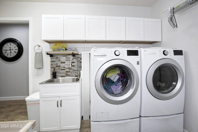 laundry room with cabinet space, baseboards, wood finished floors, washing machine and clothes dryer, and a sink