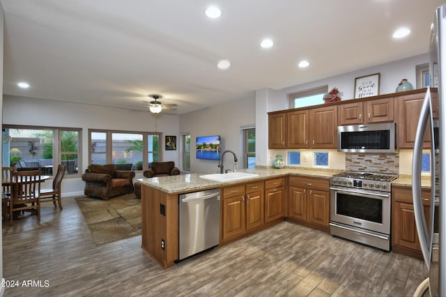 kitchen featuring light stone counters, tasteful backsplash, appliances with stainless steel finishes, a sink, and a peninsula