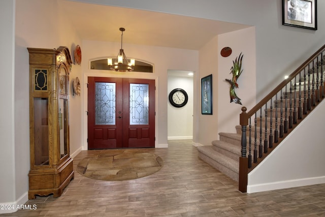 foyer entrance with french doors, stairway, wood finished floors, a chandelier, and baseboards