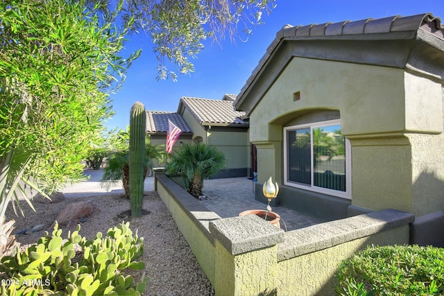 view of side of home featuring a tiled roof, a patio area, and stucco siding