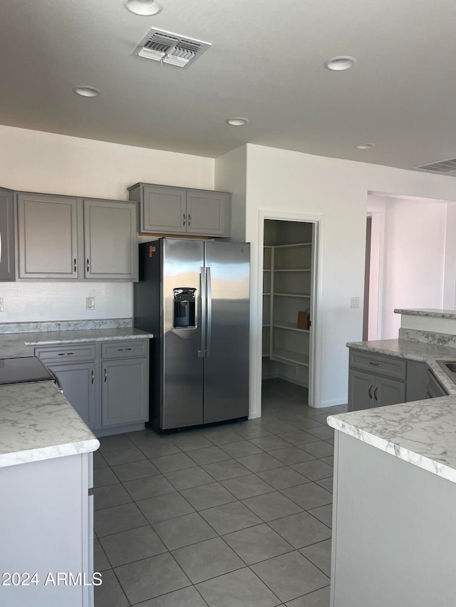 kitchen with stainless steel fridge, light tile patterned floors, and gray cabinetry