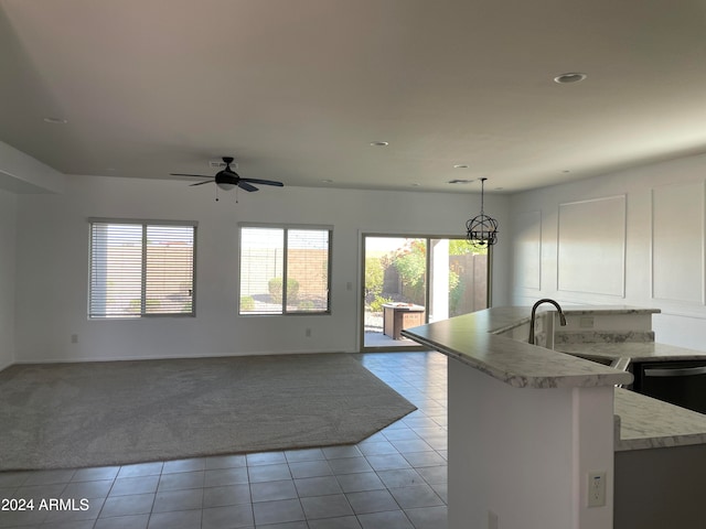 kitchen with kitchen peninsula, sink, ceiling fan with notable chandelier, pendant lighting, and light colored carpet