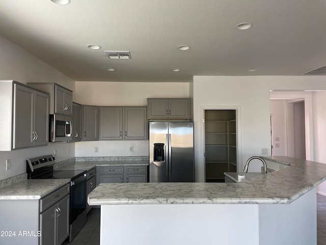 kitchen with appliances with stainless steel finishes, a center island, tile patterned floors, and gray cabinetry