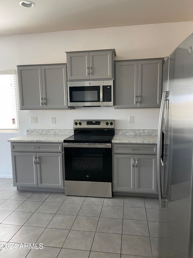 kitchen featuring appliances with stainless steel finishes, light tile patterned flooring, light stone counters, and gray cabinetry