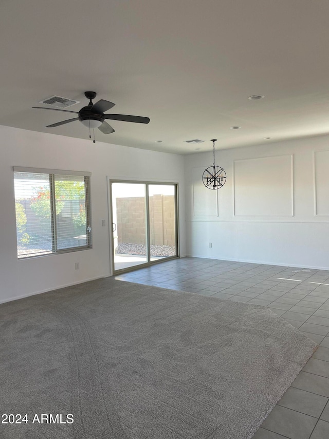 carpeted spare room featuring ceiling fan with notable chandelier