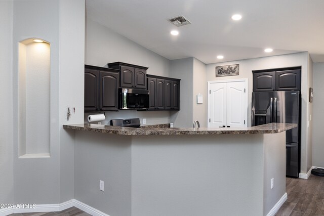 kitchen with appliances with stainless steel finishes, kitchen peninsula, dark hardwood / wood-style floors, and dark stone counters