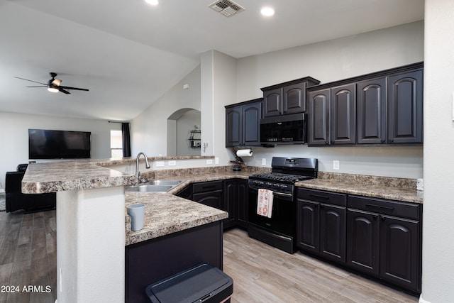 kitchen featuring black gas range, a kitchen breakfast bar, kitchen peninsula, sink, and light wood-type flooring