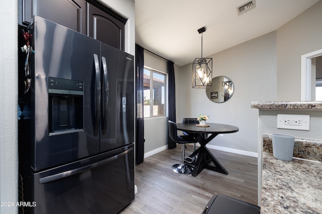 kitchen featuring lofted ceiling, dark brown cabinetry, black fridge with ice dispenser, light stone counters, and light hardwood / wood-style floors