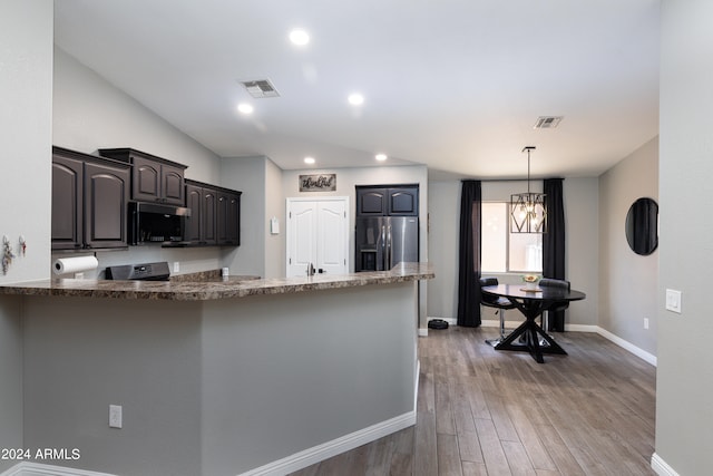 kitchen with hardwood / wood-style flooring, kitchen peninsula, stainless steel appliances, dark stone countertops, and a notable chandelier