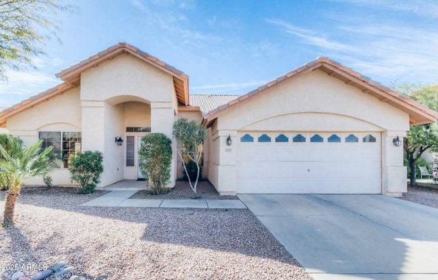 mediterranean / spanish-style home with stucco siding, a garage, driveway, and a tiled roof