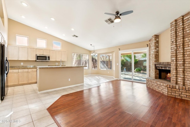 kitchen featuring visible vents, a ceiling fan, light brown cabinets, stainless steel microwave, and a brick fireplace