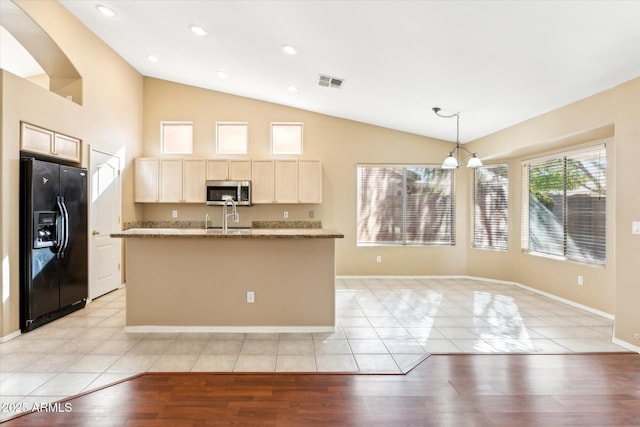 kitchen with light brown cabinets, visible vents, a sink, stainless steel microwave, and black refrigerator with ice dispenser