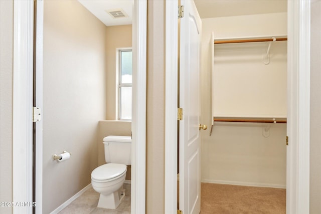 bathroom featuring visible vents, toilet, a walk in closet, and baseboards