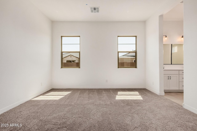 unfurnished bedroom featuring baseboards, connected bathroom, visible vents, and light carpet