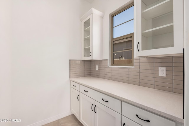 kitchen featuring light tile patterned flooring, backsplash, glass insert cabinets, baseboards, and white cabinets