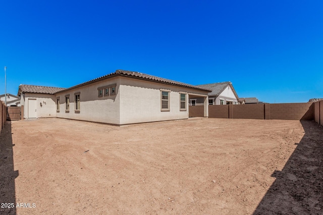 back of property featuring a fenced backyard, a tiled roof, and stucco siding