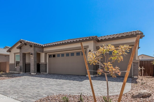 view of front of property with stucco siding, fence, a tiled roof, decorative driveway, and a garage