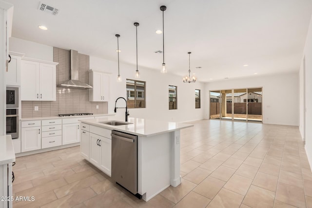 kitchen featuring dishwasher, a sink, wall chimney range hood, gas stovetop, and a notable chandelier