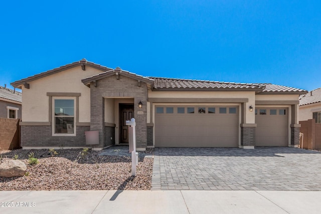 view of front of property featuring stucco siding, a tiled roof, decorative driveway, brick siding, and a garage