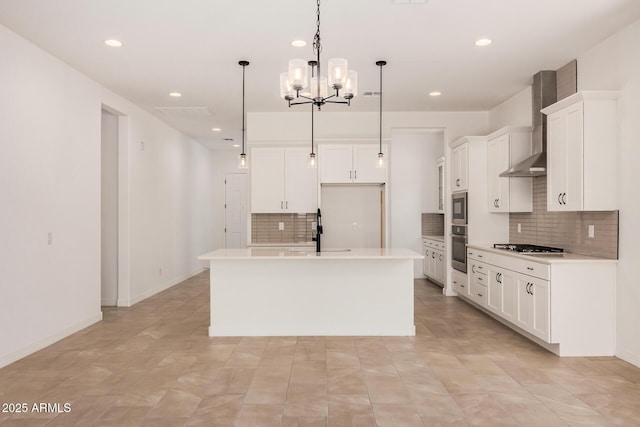 kitchen featuring a kitchen island with sink, wall chimney exhaust hood, stainless steel appliances, a sink, and an inviting chandelier