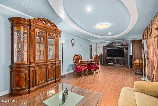 interior space with a raised ceiling, a textured ceiling, baseboards, and wood finished floors