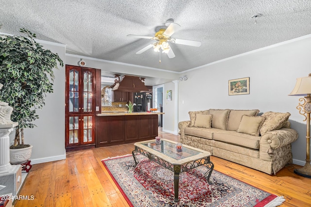 living area featuring light wood finished floors, decorative columns, ceiling fan, ornamental molding, and a textured ceiling