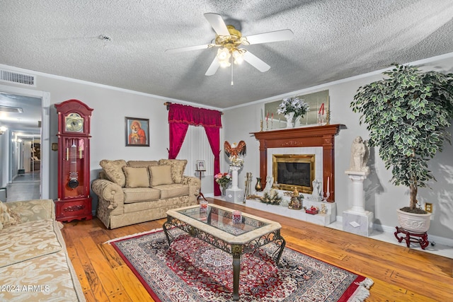 living room with ornamental molding, a glass covered fireplace, visible vents, and hardwood / wood-style flooring