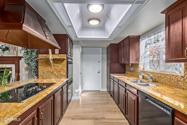 kitchen featuring decorative backsplash, a raised ceiling, black appliances, premium range hood, and a sink