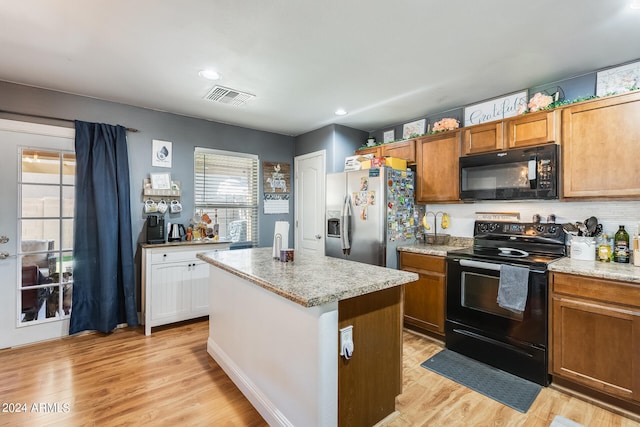 kitchen featuring light wood-type flooring, black appliances, a kitchen island, and tasteful backsplash