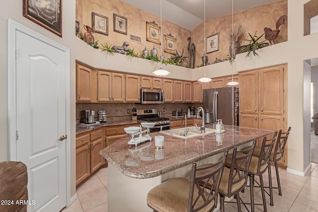 kitchen featuring pendant lighting, stainless steel appliances, a kitchen island with sink, high vaulted ceiling, and light tile patterned floors