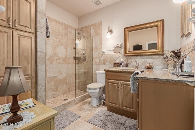 bathroom featuring toilet, vanity, tile walls, tile patterned flooring, and a tile shower