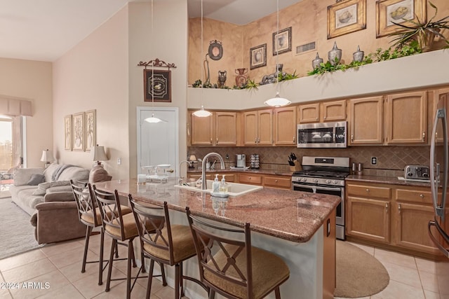 kitchen with high vaulted ceiling, light tile patterned floors, appliances with stainless steel finishes, and a breakfast bar area