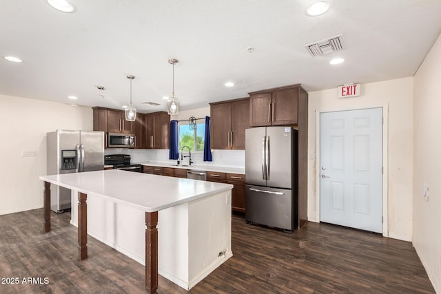 kitchen with appliances with stainless steel finishes, a center island, hanging light fixtures, light countertops, and a sink