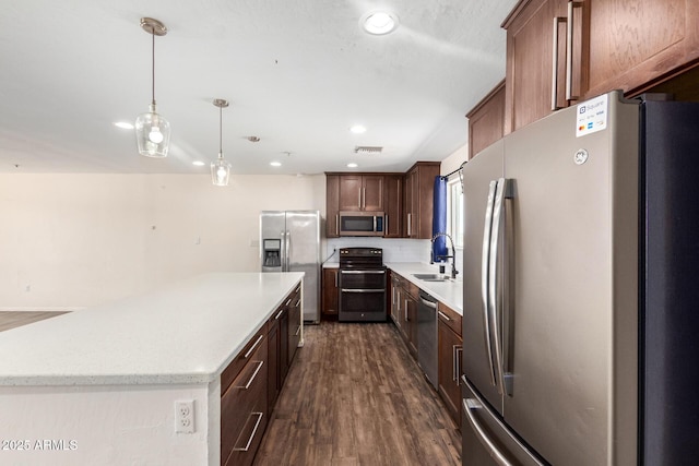 kitchen with a sink, stainless steel appliances, light countertops, and decorative light fixtures