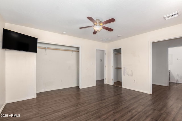 unfurnished bedroom with two closets, baseboards, visible vents, and dark wood-type flooring