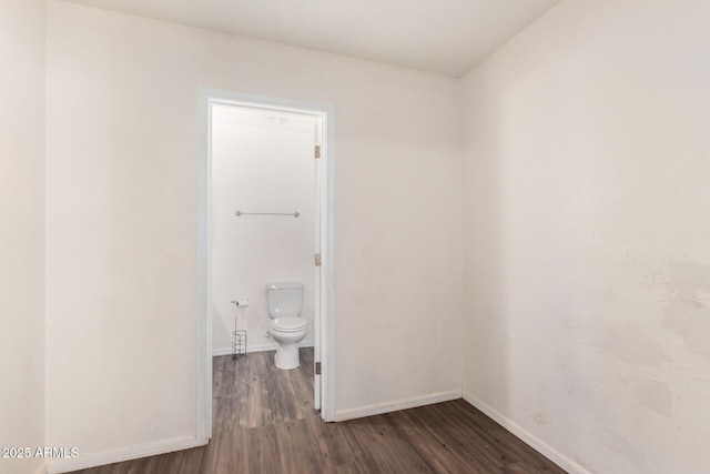 spare room with baseboards and dark wood-type flooring