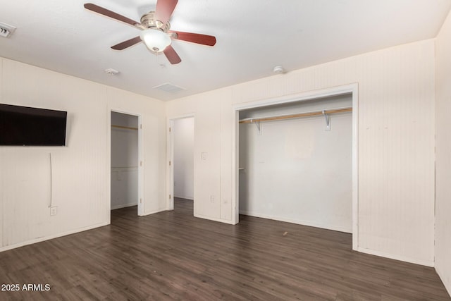 unfurnished bedroom featuring visible vents, baseboards, dark wood finished floors, a ceiling fan, and two closets