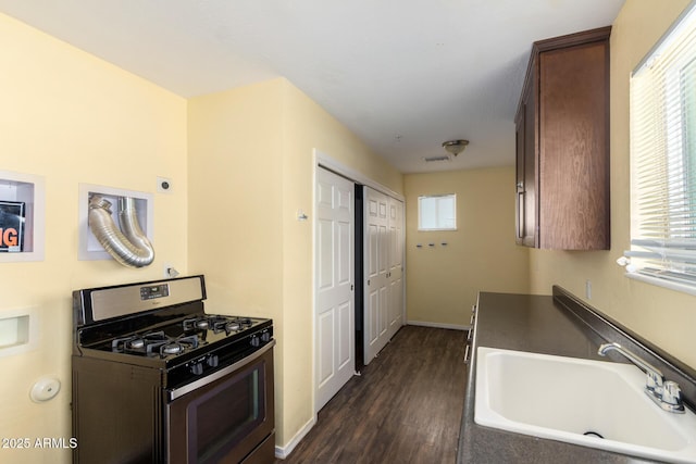 kitchen featuring dark countertops, gas range, dark brown cabinetry, and a sink