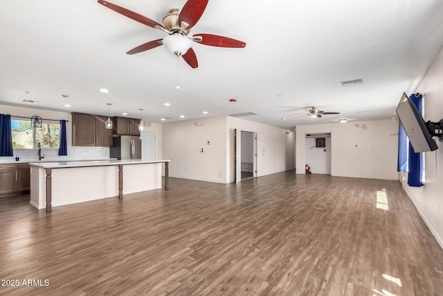 unfurnished living room with ceiling fan, visible vents, dark wood finished floors, and a sink